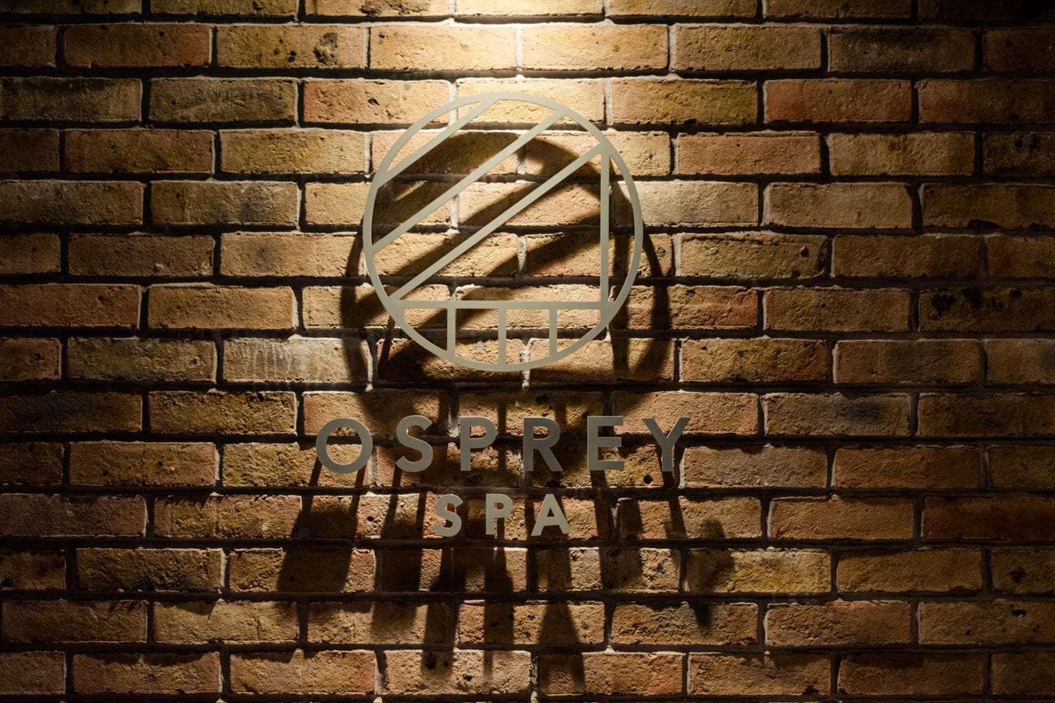 Osprey Spa logo on a brick wall with shadow effect.